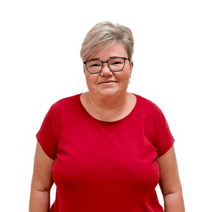 Portrét usmívající se ženy v brýlích a červeném tričku s krátkými světlými vlasy na bílém pozadí.